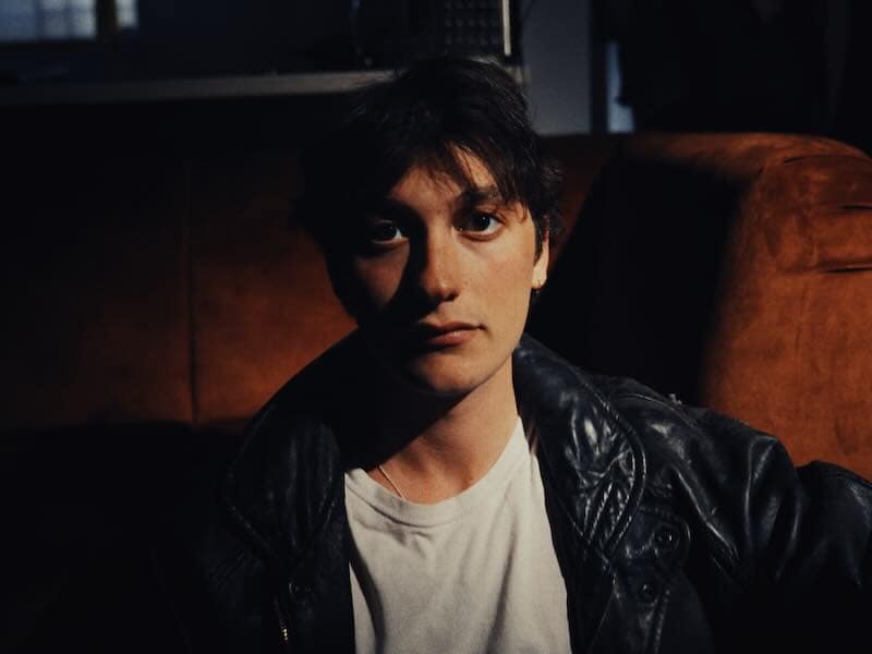 Portrait of YONAH, indie-rock artist, in a dark setting with leather jacket.